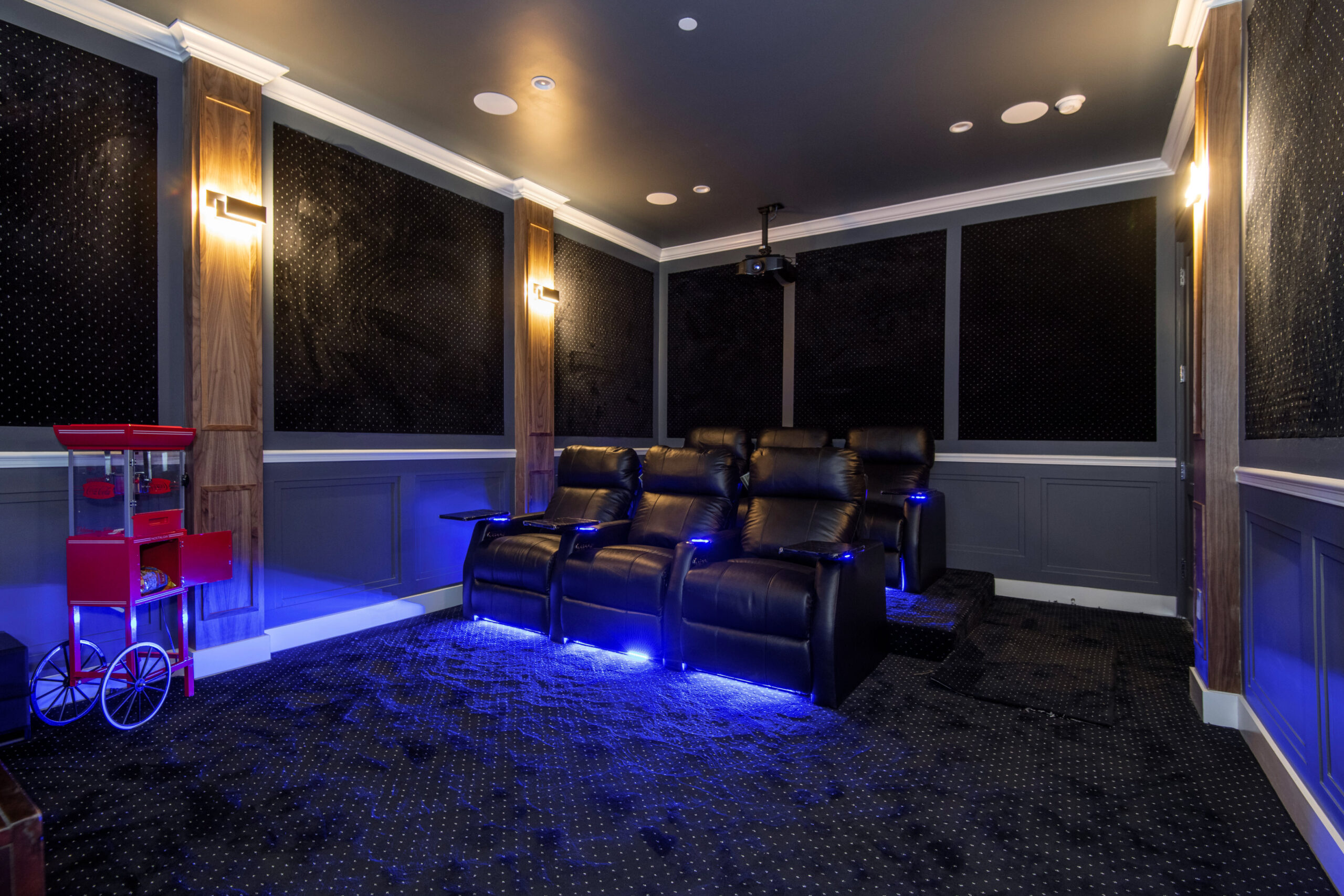 Blue lit home theater with black leather sofa and red cart