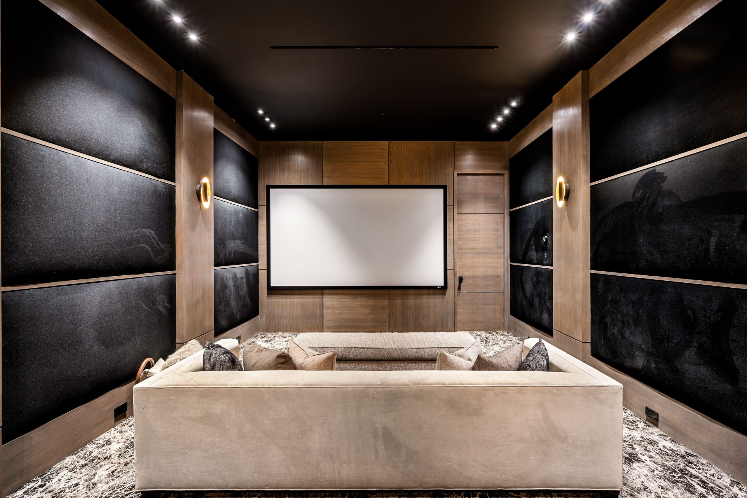 A modern home theater room with comfortable seating, a large screen, and elegant wood paneling and black acoustic walls.