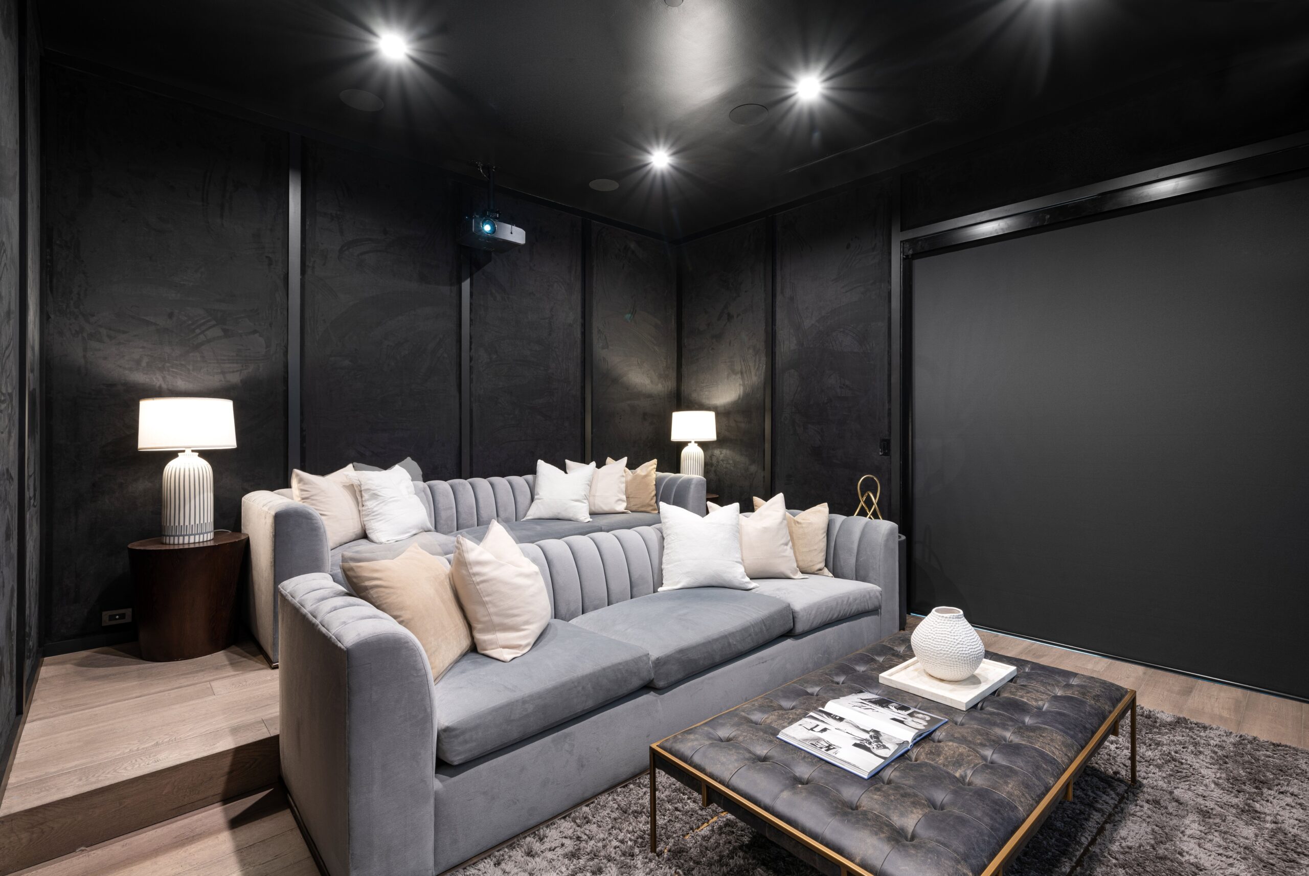 Modern home theater room with a gray sofa, pillows, and ambient lighting, creating a cozy atmosphere.